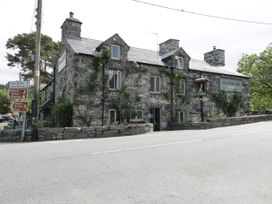 A stone building with climbing plants and multiple chimneys by a roadside with directional signs at Glandwr Cottage in Llanbedr