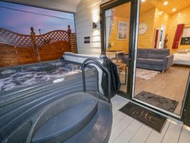 An outdoor hot tub next to a sliding glass door leading to a wooden interior with a sofa and a bed at Binevanagh Cabin in Magilligan near Castlerock