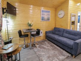 A small living room with blue sofa gray rug wall clock small table with two chairs and a wall mounted TV at Binevanagh Cabin Magilligan near Castlerock