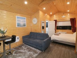 A wooden cabin interior with a sofa, bed, dining table with chairs, wall clock, and a framed picture at Binevanagh Cabin Magilligan near Castlerock