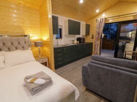 A cabin interior with a bed and bedside table lamp a kitchenette with cabinets and a sink a gray sofa and sliding glass doors at Binevanagh Cabin in Magilligan near Castlerock