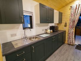 A kitchen with upper and lower cabinets a sink a kettle a toaster oven and a floral curtain at Binevanagh Cabin in Magilligan near Castlerock
