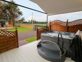 An outdoor deck with a hot tub and wooden fencing overlooking a yard and a small building at Binevanagh Cabin in Magilligan near Castlerock