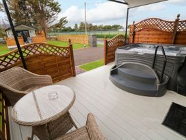 An outdoor patio with a hot tub and wicker chairs around a glass table at Binevanagh Cabin in Magilligan near Castlerock