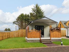 A small cabin with a covered porch and wooden fence around it on a grassy lawn at Binevanagh Cabin in Magilligan near Castlerock