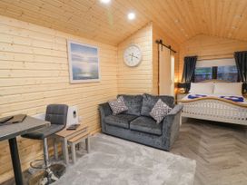 A wooden cabin interior with a sofa table and chair a bed with pillows and towels and a wall clock at MUSSENDEN CABIN Magilligan near Castlerock
