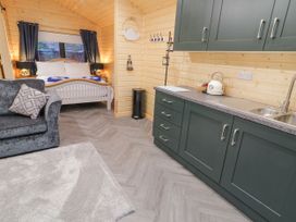 A kitchen area with dark green cabinets and a sink beside a sleeping area with a bed and black curtains at MUSSENDEN CABIN in Magilligan near Castlerock