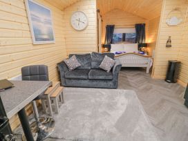 A wooden cabin interior with a grey sofa and table and stools and a bed in the background with curtains at MUSSENDEN CABIN Magilligan near Castlerock