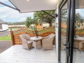 An outdoor patio with two wicker chairs and a round table with a wooden fence and garden shed in the background at MUSSENDEN CABIN Magilligan near Castlerock