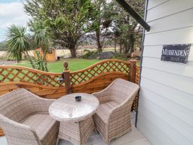 Two wicker chairs with a glass-top table on a balcony with a wooden lattice fence and trees in the background at Mussenden Cabin Magilligan near Castlerock