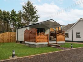 A small white cabin with a covered porch and wooden railings surrounded by grass at Benone Cabin in Magilligan near Castlerock