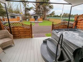 An outdoor deck with a hot tub wicker chair and wooden fence with cabins and grass in the background at Benone Cabin in Magilligan near Castlerock