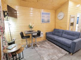 A living area with a blue sofa a small table with two chairs a wall clock and a mounted television at Benone Cabin Magilligan near Castlerock