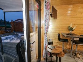 A wooden interior room with a small round table and tall chairs next to a mounted television and a hot tub outside at Benone Cabin in Magilligan near Castlerock
