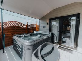 An outdoor covered deck with a hot tub, steps, wooden privacy fencing, and glass doors at Benone Cabin in Magilligan near Castlerock