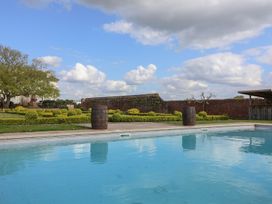 An outdoor swimming pool with two wooden barrels on the poolside and a garden with trimmed bushes and a brick wall at Buckland House and Annex in Lower Durston near Taunton