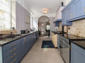 A galley kitchen with blue cabinets a double oven a stovetop and tiled backsplash at Buckland House and Annex in Lower Durston near Taunton