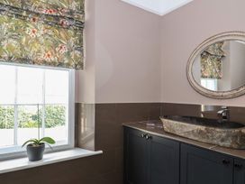 A bathroom with a stone sink a round mirror floral window blind and a potted plant on the window sill at Buckland House and Annex Lower Durston near Taunton