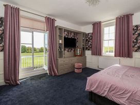 A bedroom with a bed pink bedding built in storage with a tv purple curtains and windows overlooking green fields at Buckland House and Annex Lower Durston near Taunton
