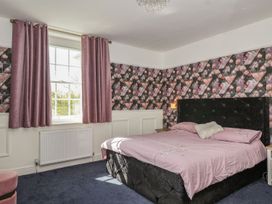 A bedroom with a large bed purple sheets pink curtains and floral patterned wallpaper at Buckland House and Annex Lower Durston near Taunton