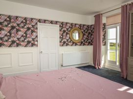 A bedroom with a bed and patterned wallpaper and a door and window with pink curtains at Buckland House and Annex in Lower Durston near Taunton