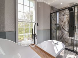 A bathroom with a freestanding bathtub a wooden bath tray a black faucet a window and a walk in shower with marble walls at Buckland House and Annex Lower Durston near Taunton