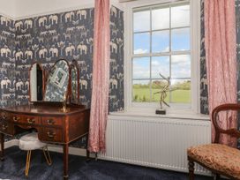 A room with a wooden dressing table with a tri-fold mirror a gray stool a window with pink curtains and a sculpture on the radiator at Buckland House and Annex in Lower Durston near Taunton