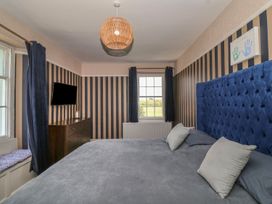 A bedroom with a large bed with gray bedding and blue headboard and a dresser with a television and windows at Buckland House and Annex in Lower Durston near Taunton