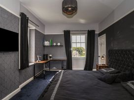 A bedroom with a black bed a wooden desk under a window and black curtains at Buckland House and Annex Lower Durston near Taunton