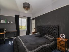 A bedroom with a large bed black bedding two wooden nightstands and a desk near a window at Buckland House and Annex in Lower Durston near Taunton