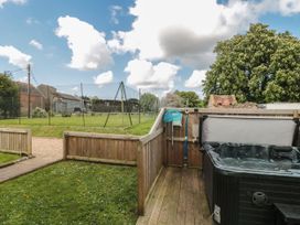 An outdoor area with a fenced hot tub on a wooden deck and a grassy lawn with a chain link fence at Buckland House and Annex in Lower Durston near Taunton