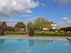 A swimming pool with garden bushes and a tree in front of a house at Buckland House and Annex in Lower Durston near Taunton