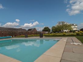 An outdoor swimming pool with a net skimmer on the side and a house with trees in the background at Buckland House and Annex in Lower Durston near Taunton