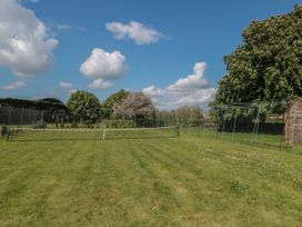 An outdoor badminton court with a net on a grassy area surrounded by trees and a metal fence at Buckland House and Annex in Lower Durston near Taunton