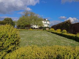 A garden with bushes and a lawn with small white flowers and a house and brick wall in the background at Buckland House and Annex Lower Durston near Taunton