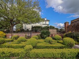 A garden with trimmed hedges and a tree beside a metal fence and a large white house at Buckland House and Annex in Lower Durston near Taunton