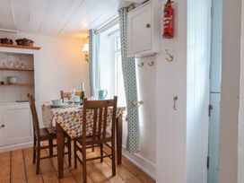 A dining area with a wooden table and chairs set near a window with patterned curtains at Teana Cottage in Polperro