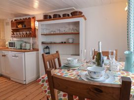A kitchen dining area with a wooden table set with plates bowls glasses and a bottle in Teana Cottage Polperro
