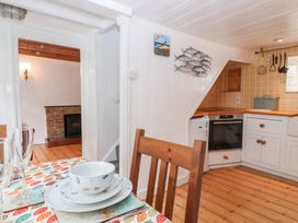 A kitchen with white cabinets and wooden floor with a dining table set with dishes and glasses at Teana Cottage in Polperro