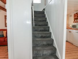 A carpeted staircase surrounded by white walls with a kitchen on the right and a living area with a red sofa on the left at Teana Cottage in Polperro