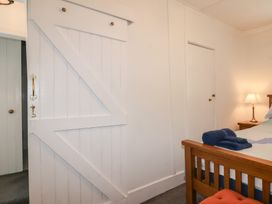 A bedroom with a wooden bed frame a bedside table with a lamp folded towels and white doors at Teana Cottage in Polperro