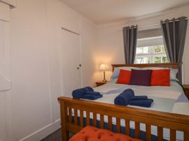 A bedroom with a wooden bed with folded towels on it two bedside tables with a lamp and window with curtains at Teana Cottage in Polperro