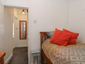 A bedroom with a wooden bed with patterned bedding and orange pillows and a narrow hallway with a wall mirror at Teana Cottage Polperro