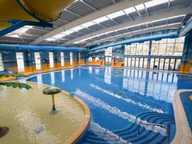 An indoor swimming pool with a seating area a waterslide and large windows at Ripples & Reeds - Billing Aquadrome in Billing Aquadrome Holiday Park