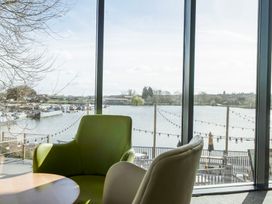 A room with two chairs and a round wooden table facing large windows overlooking a marina and lake at Ripples & Reeds - Billing Aquadrome in Billing Aquadrome Holiday Park
