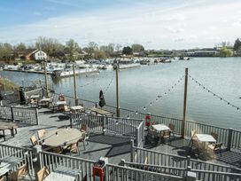 An outdoor seating area with tables and chairs next to water with boats docked at a marina at Ripples & Reeds - Billing Aquadrome in Billing Aquadrome Holiday Park