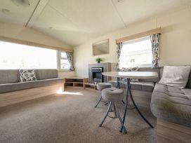 A sitting area with built-in sofas a small table with three stools a fireplace and windows with curtains at Ripples & Reeds - Billing Aquadrome in Billing Aquadrome Holiday Park