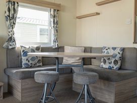 A dining area with a wooden table surrounded by gray cushioned bench seating and two stools at Ripples & Reeds - Billing Aquadrome in Billing Aquadrome Holiday Park