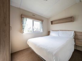 A bedroom with a double bed white bedding wooden headboard a window with curtains and a wooden wardrobe at Ripples & Reeds - Billing Aquadrome