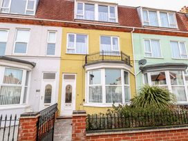 The front exterior of three attached two story houses with different colored facades and front gardens at 34 North Denes Road in Great Yarmouth